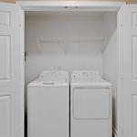 Compact laundry area with modern washer and dryer, enhanced by sleek white tones and handy storage shelving.