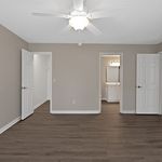 Modern bedroom with sleek wood flooring, elegant ceiling fan, and en-suite bathroom, offering bright and inviting space.