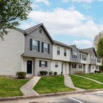 Charming townhouse complex with modern siding, lush green lawns, and peaceful suburban setting under a bright blue sky.