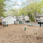 Charming apartment community features a cozy fenced yard with benches, surrounded by lush green trees and attractive residential buildings.