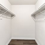 Spacious walk-in closet with white walls and elegant hardwood flooring, perfect for ample storage.