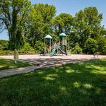 Charming playground nestled in a lush green park, featuring vibrant slides and climbing structures under a clear blue sky.