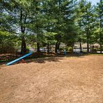 Charming dog park with tall trees, a blue seesaw, and playful exercise equipment, perfect for pet-friendly living.