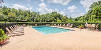 Inviting outdoor pool area with lounge chairs and seating, surrounded by lush greenery under a bright blue sky.