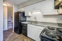 Modern kitchen with sleek countertops, white cabinetry, and black appliances, leading to cozy carpeted stairs.