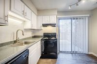 Modern kitchen with sleek white cabinets, granite countertops, and stainless steel fixtures, opening to a sunlit patio through elegant vertical blinds.