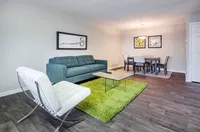 Contemporary living and dining area with sleek furniture, vibrant green rug, and elegant artwork.