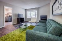 Chic living room with a modern green sofa, glass coffee table, and a view into the kitchen, perfect for stylish relaxation.