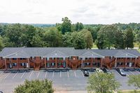 Charming brick apartment complex set amid lush greenery, featuring convenient parking and inviting balconies.
