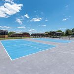 Vibrant outdoor sports courts under a clear blue sky, surrounded by lush greenery and modern apartment buildings.