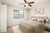 Elegant bedroom featuring a cushioned headboard bed, large window with garden view, and modern ceiling fan.