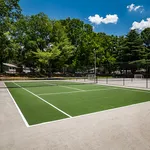 Inviting outdoor tennis court surrounded by lush greenery and clear blue skies, ideal for recreational sports and fitness enthusiasts.