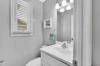Modern bathroom with sleek white vanity, polished fixtures, and natural light streaming through a window with blinds.