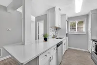 Chic kitchen with modern white cabinetry, elegant countertops, stainless steel appliances, and natural light streaming through a large window.