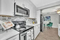 Modern kitchen with sleek stainless steel appliances, elegant white cabinetry, stylish backsplash, and an inviting adjacent dining area with vibrant green chairs.