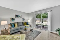 Inviting living room with stylish decor, featuring a cozy gray sofa, vibrant cushions, and a large glass door opening to a charming patio.
