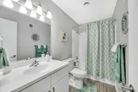 Elegant bathroom featuring a sleek white vanity, modern fixtures, and a soothing green color theme with patterned shower curtain and matching towels.
