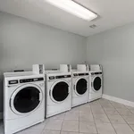 Modern laundry room with four sleek white washing machines set against a calming light grey wall, perfect for convenient living.