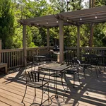 Charming outdoor patio with wooden decking and elegant iron furniture, surrounded by lush greenery and featuring a cozy pergola with string lights, perfect for entertaining.