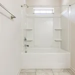 Modern bathroom with pristine white bathtub and shower, accented by elegant tile flooring and natural light from a frosted window.