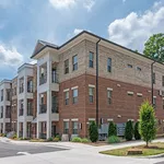 Elegant brick apartment building with classic balconies and lush landscaping, bathed in natural sunlight.