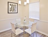 Chic dining area with a modern glass table, stylish white chairs, and elegant wall art, basking in natural light.