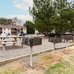 Charming apartment complex with outdoor picnic area and barbecue grills under lush green trees.