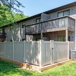 Charming apartment exterior with a cozy balcony and modern wood paneling, surrounded by lush greenery and a stylish fence.