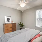 Cozy bedroom with modern ceiling fan, natural light, stylish dresser, and accent plant creating a serene atmosphere.