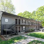 Charming two-story apartment building surrounded by lush greenery, featuring modern exterior and ample parking space.
