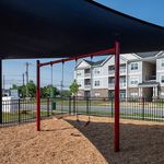 Inviting modern apartment complex with a charming playground featuring swings and a shaded area, perfect for family-friendly living.