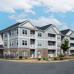 Modern three-story apartment building with elegant balconies, surrounded by lush greenery and spacious parking.