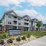 Charming North Main Village apartment homes with modern architecture, landscaped gardens, and inviting balconies under a clear blue sky.
