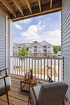 Inviting balcony view from a charming apartment, featuring cozy seating and scenic outlooks over a modern residential complex against a bright, blue sky.