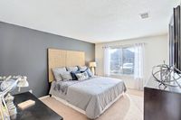 Bright and inviting bedroom with a stylish grey and beige decor, featuring a large window allowing natural light, and a comfortable bed with decorative pillows that creates a cozy atmosphere.