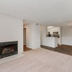 Inviting apartment interior with a cozy fireplace, plush carpeting, and an open kitchen layout featuring modern appliances, perfect for comfortable living.