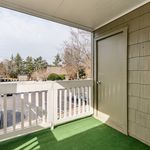 Charming apartment balcony with green artificial grass and scenic view of trees and open sky.