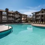 Inviting apartment complex with a sparkling outdoor pool, surrounded by modern architecture and poolside lounge chairs under a clear blue sky.