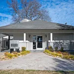 Charming leasing center with a welcoming facade, surrounded by landscaped greenery and a paved entrance, under a bright blue sky.