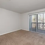 Bright apartment room with plush carpet and large sliding glass doors opening to a serene private balcony.