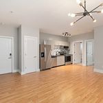 Modern open-plan kitchen and living area with sleek stainless steel appliances, wooden flooring, and stylish lighting fixtures.