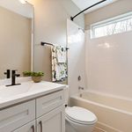Elegant bathroom with white cabinetry, stylish fixtures, and a well-lit bathtub area featuring a modern shower.