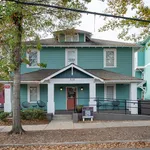 Charming teal-painted house with a welcoming front porch and stylish seating, surrounded by mature trees and vibrant greenery.