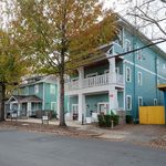 Charming teal apartment building with a spacious front porch, nestled among mature trees and a quiet neighborhood street.