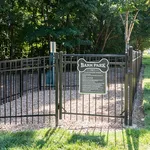 Inviting fenced Bark Park with plush grassy surroundings and shaded areas, perfect for pet playtime and relaxation.