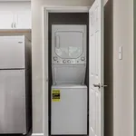 Convenient in-unit laundry with modern stacked washer and dryer beside a sleek stainless steel refrigerator.