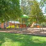 Vibrant playground with swings and slides nestled in a lush, green community setting, ideal for family-friendly living.