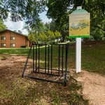 Charming apartment exterior with lush greenery, bike rack, and informational sign in a serene setting.