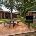 Charming apartment complex featuring lush greenery, picnic area with benches, and outdoor barbecue space.