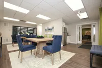 Elegant dining space with plush blue chairs and wooden table, near modern kitchen with stainless steel appliances.